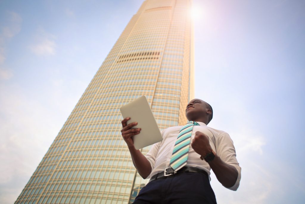 A business man with a tablet standing in front of a skyscraper