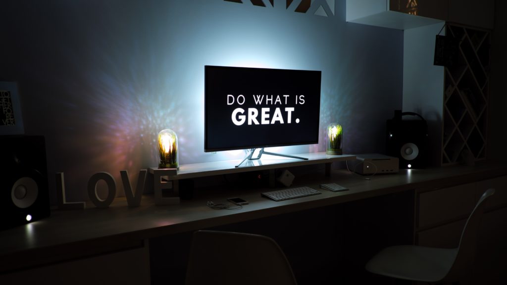 A desktop monitor in a darkened room that says do what is great.