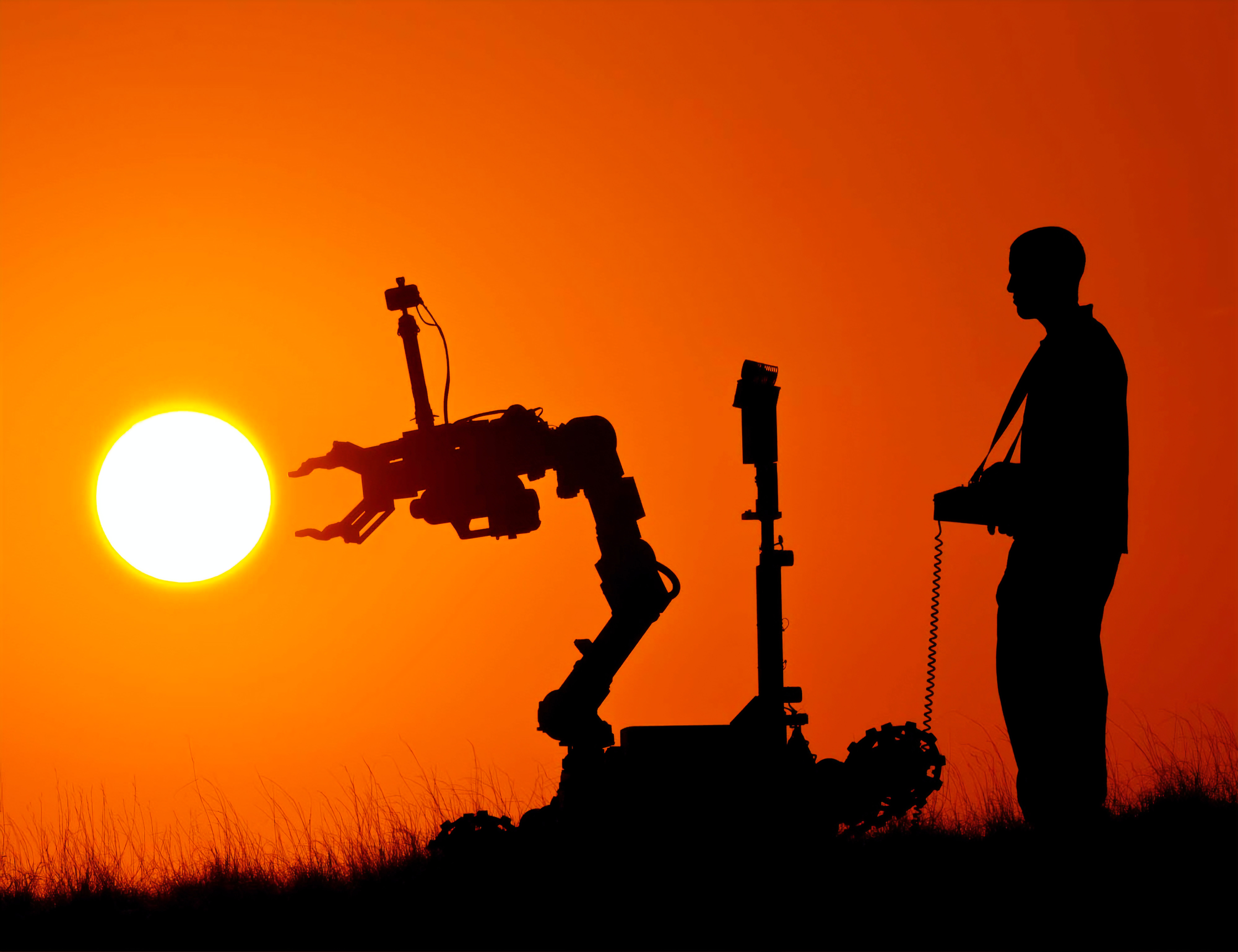 Man with a robotic controlling a robotic arm standing in front of red sky at sunset