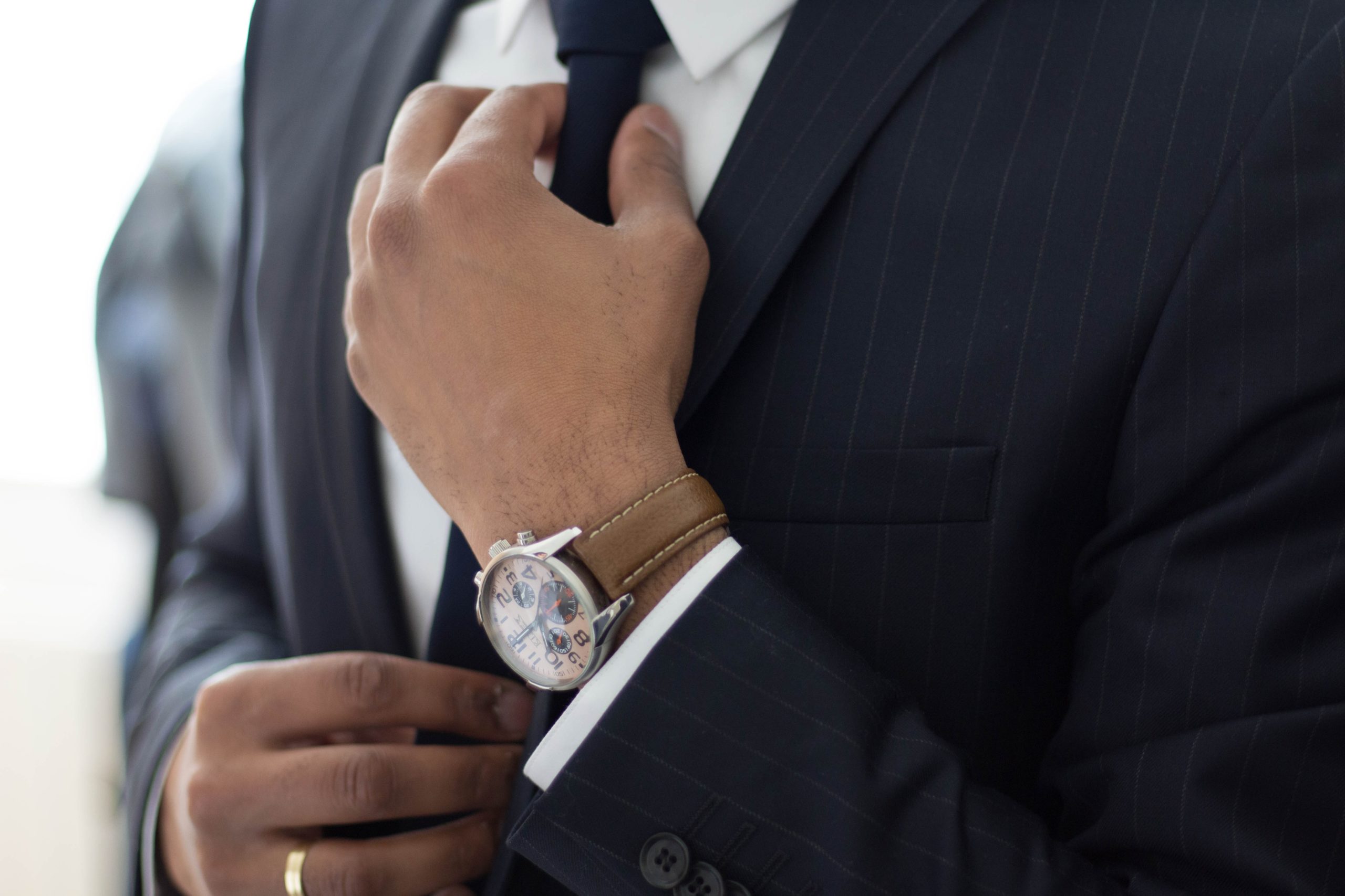 A business man in a black pinstripe suit and tie and a leather strap watch