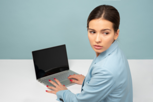 Concerned looking woman looking behind her while typing on a laptop