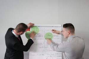 Two Men placing green circles on butchers paper in front of a grey wall
