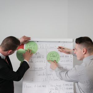 Two Men placing green circles on butchers paper in front of a grey wall